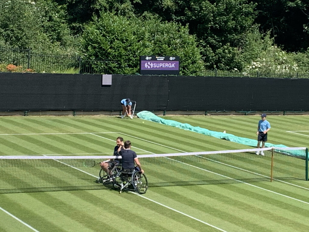 Two wheelchair tennis players high five at the net after their match on the grass courts of Edgbaston Priory Club