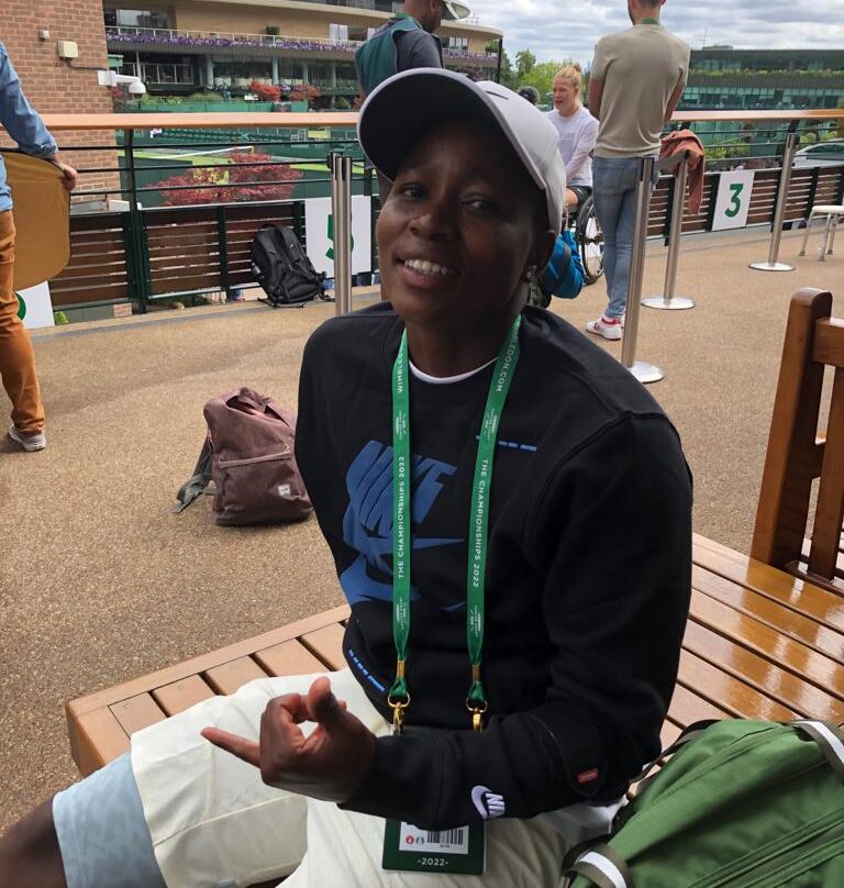 KG Montjane attends the media hour at Wimbledon 2022 and sits on the bench on the media balcony which has the view of Centre Court in the background